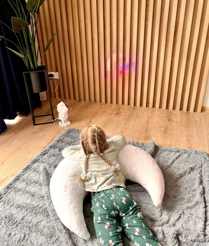 Child lying back on oversized white moon pillow, showing plush faux fur texture