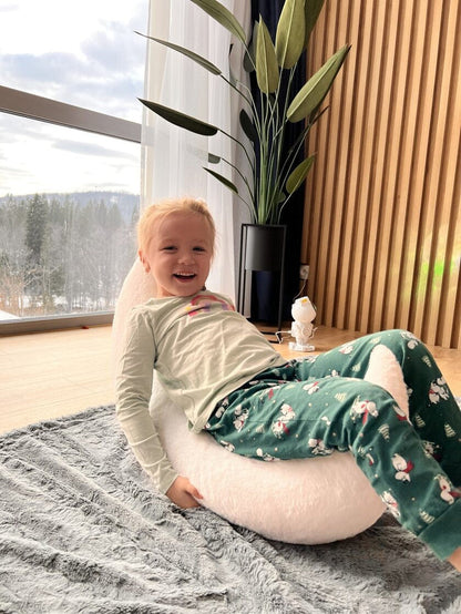 Young child sitting on white half-moon pillow by window, enjoying cozy playtime