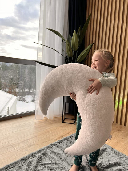 Toddler holding and hugging giant white moon pillow, demonstrating generous size