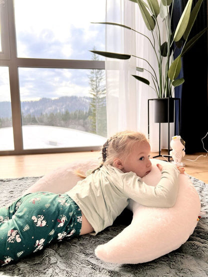 Baby resting on oversized white plush moon pillow during playtime on rug