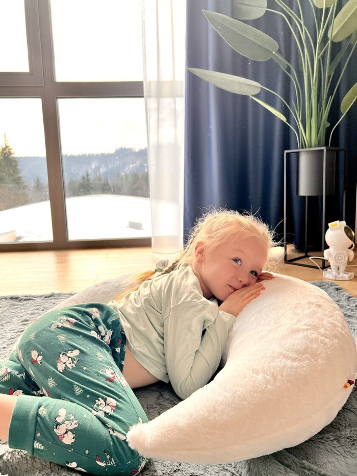Young child snuggling into white half-moon pillow, showing comfort and softness