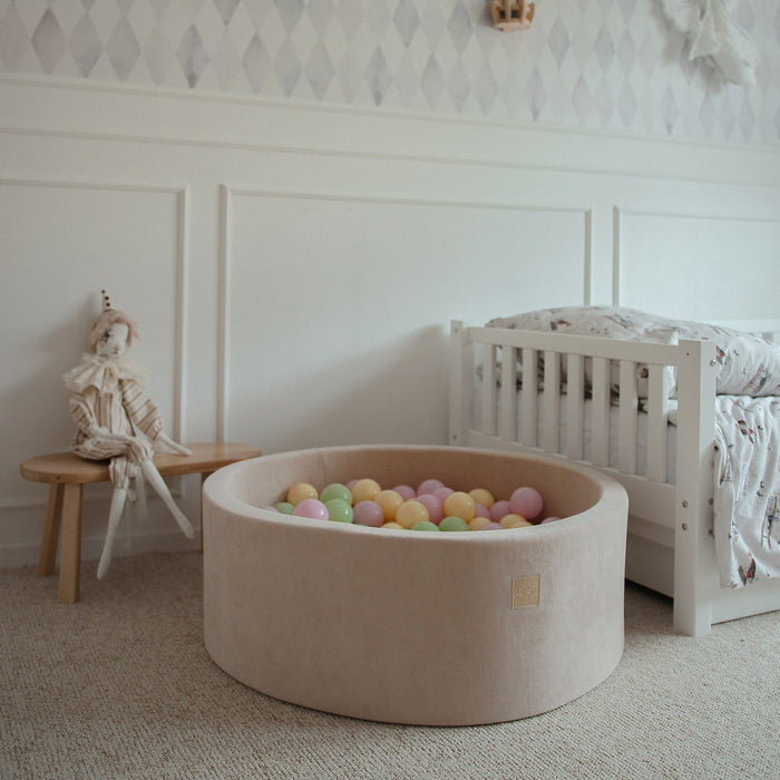 Beige foam ball pit with pastel colored balls in nursery bedroom setting