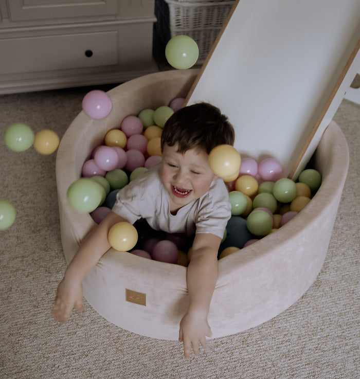 Toddler playing and laughing inside beige foam ball pit with colorful balls