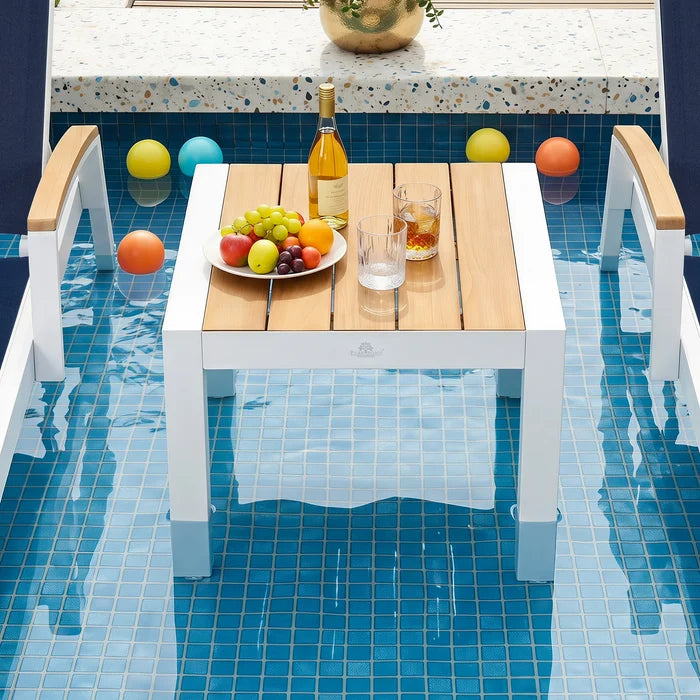 Top-down view of Peak Home Furnishings luxury teak top pool table styled with wine and fruit, floating inside a tiled swimming pool.